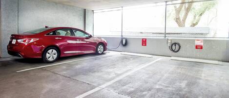 A red car parked in an electric vehicle charging station, with a concrete floor and a windowed wall.