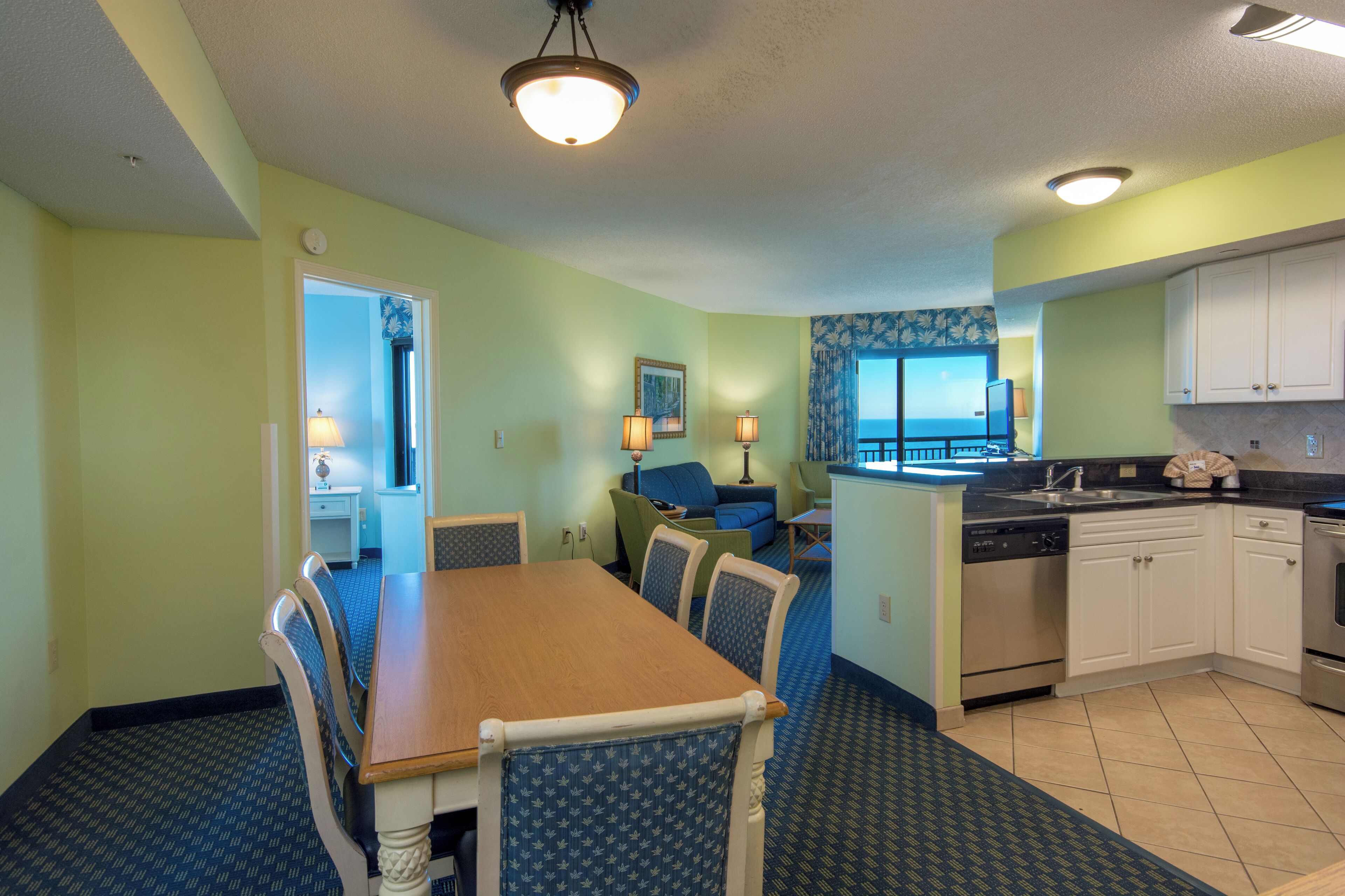 A compact kitchen with a dining area, featuring a wooden table and chairs, a dishwasher, and a stove.