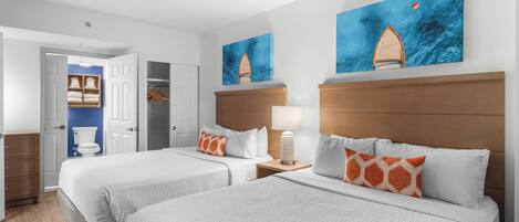 A hotel room with two beds, a wooden headboard, a nightstand with a lamp, and artwork on the walls.