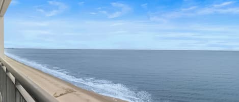 A beach view from a balcony with a railing, ocean, and clear sky.