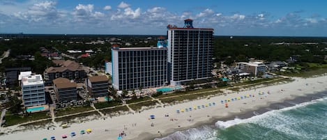 A beachfront hotel with multiple buildings, a beach with umbrellas, and ocean waves.