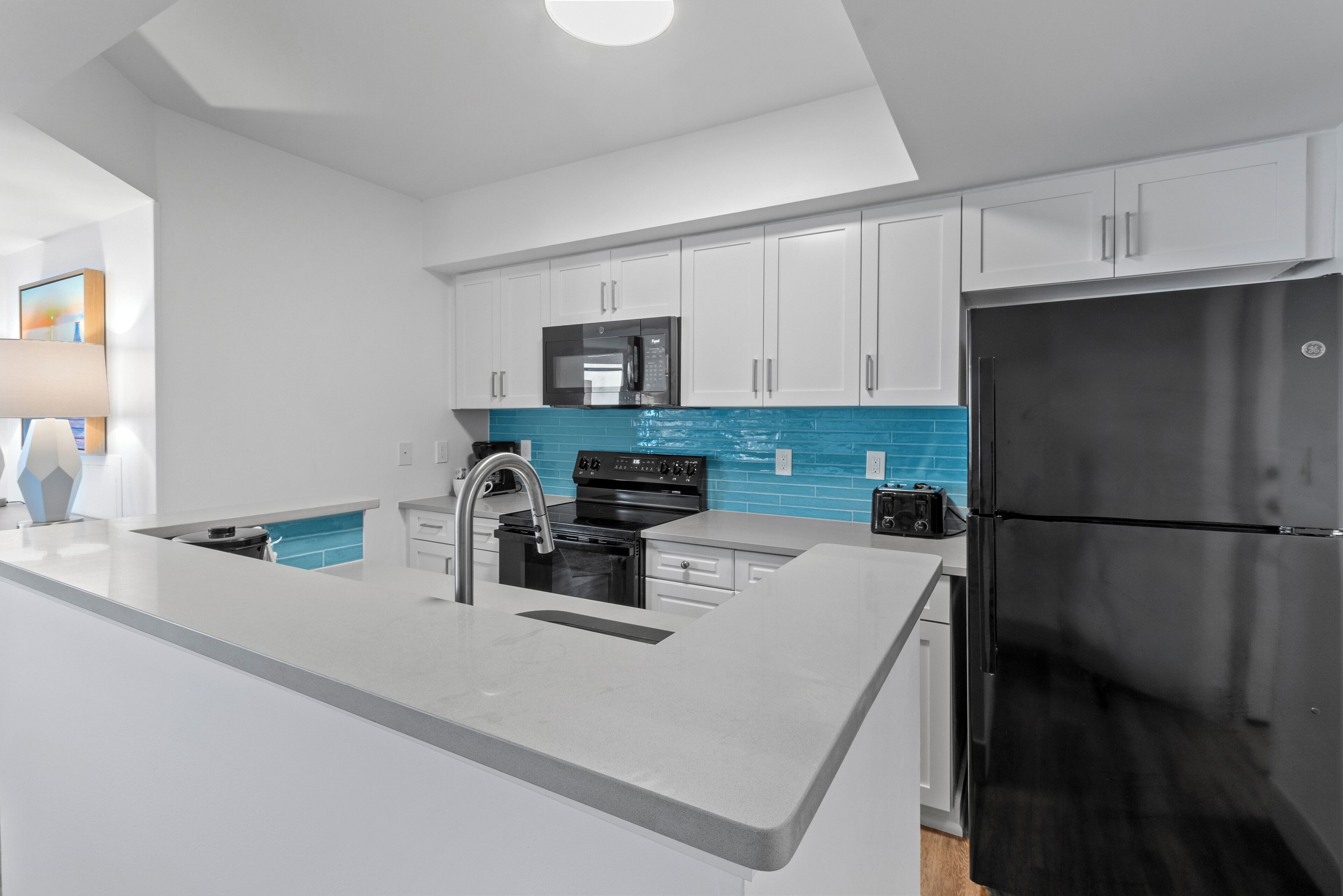 A modern kitchen with white cabinets, a black refrigerator, and a blue backsplash.