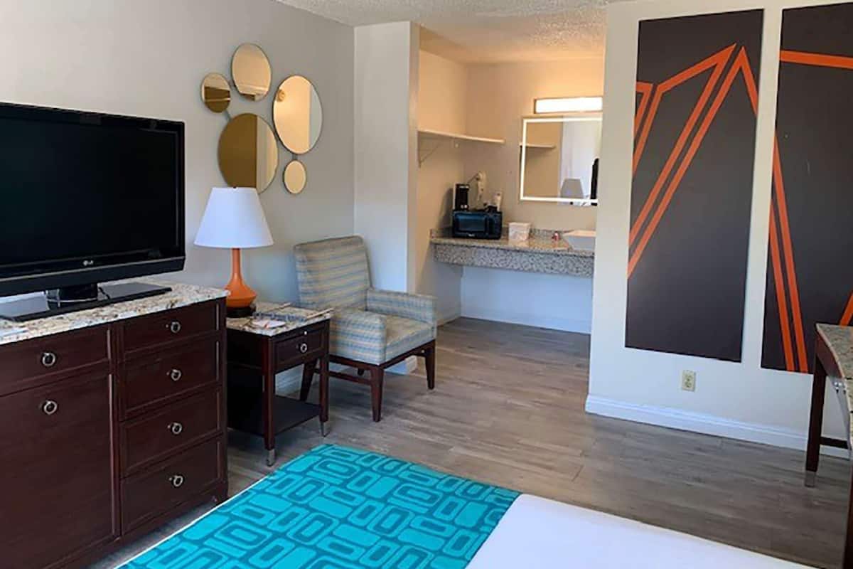 A hotel room with a flat-screen TV, a lamp, a chair, a desk, and a patterned rug.