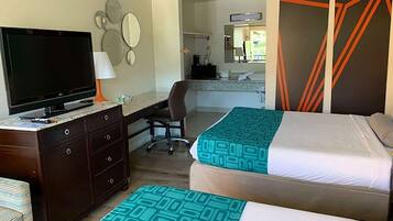 A hotel room with two beds, a desk with a TV, a chair, a dresser, and a bathroom visible in the background.