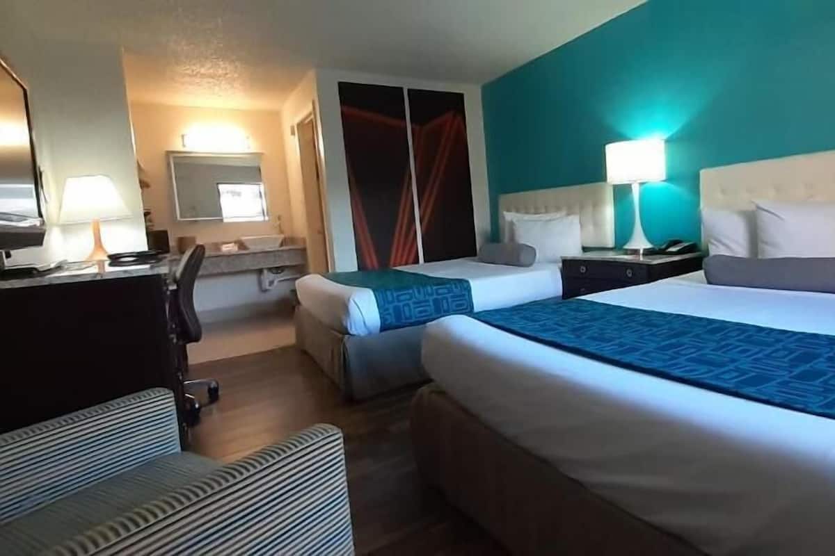 A hotel room with two beds, a desk, a chair, and a bathroom.