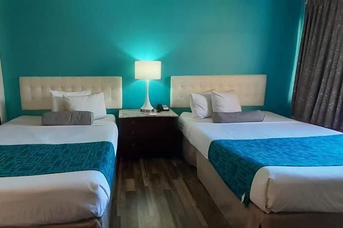 Two single beds with headboards, a nightstand with a lamp, and a teal-colored wall.