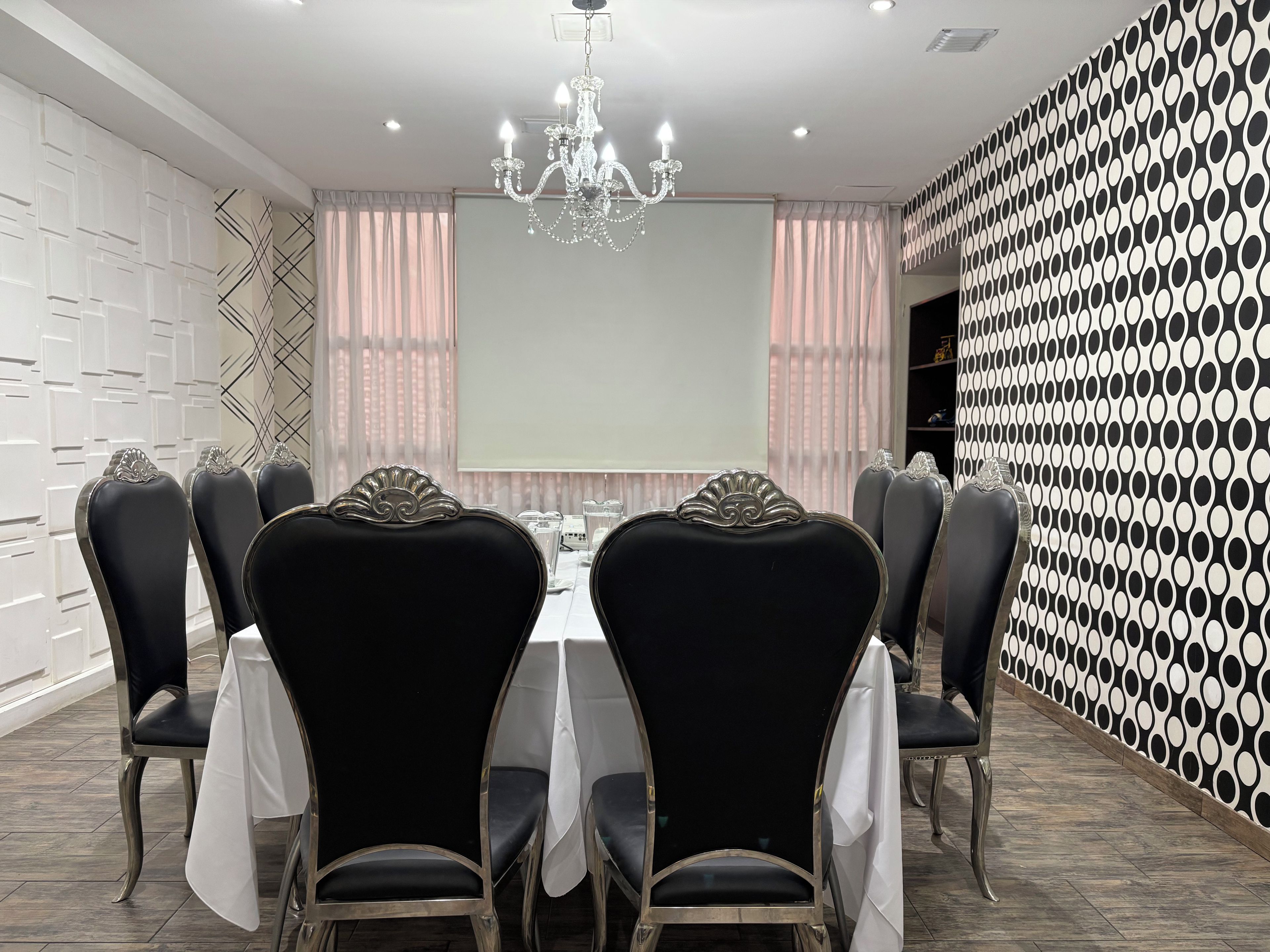 A conference room with a white table, black chairs, a chandelier, and a patterned wall.