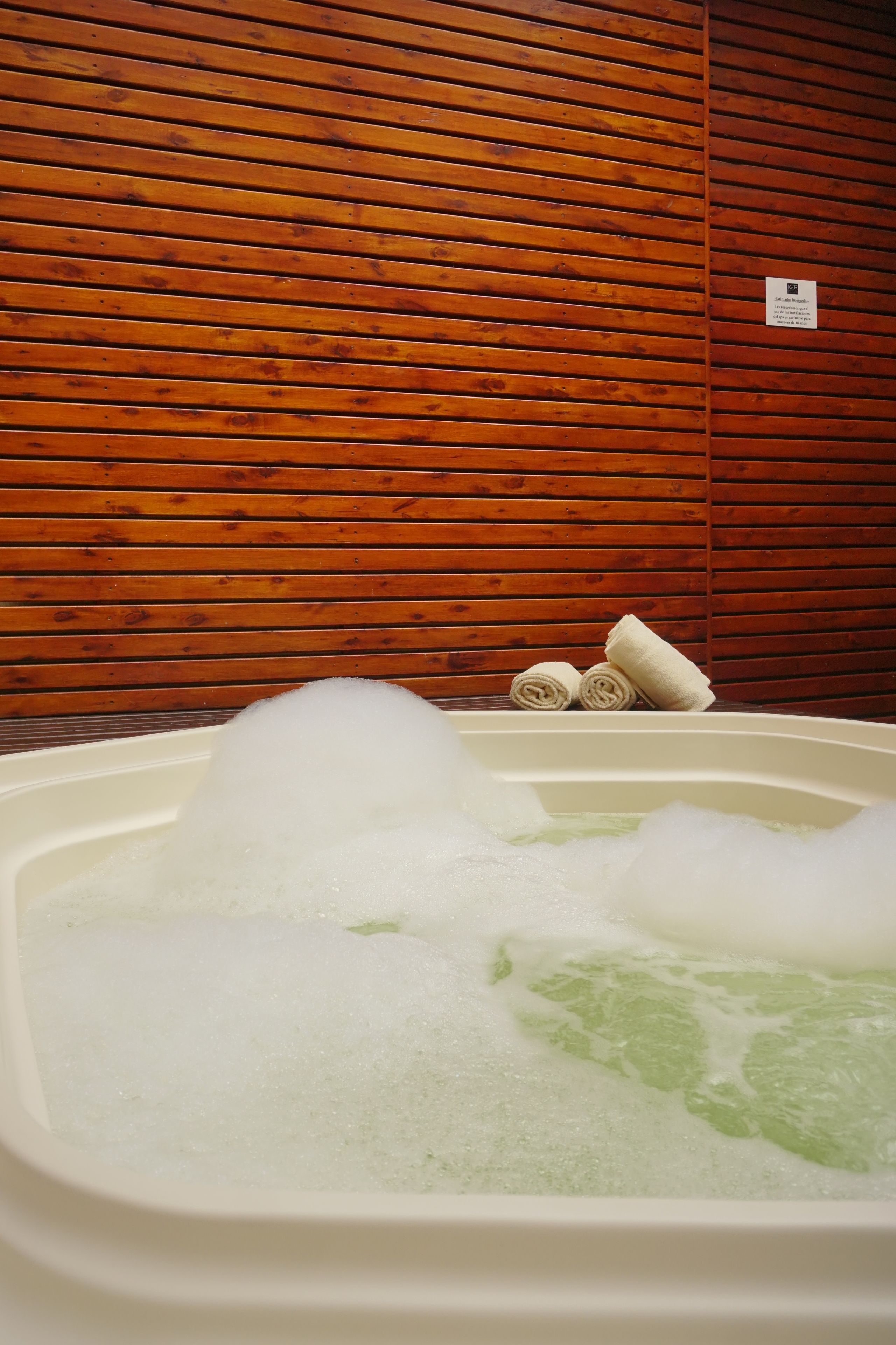 A hot tub with bubbles, a wooden wall, and towels.