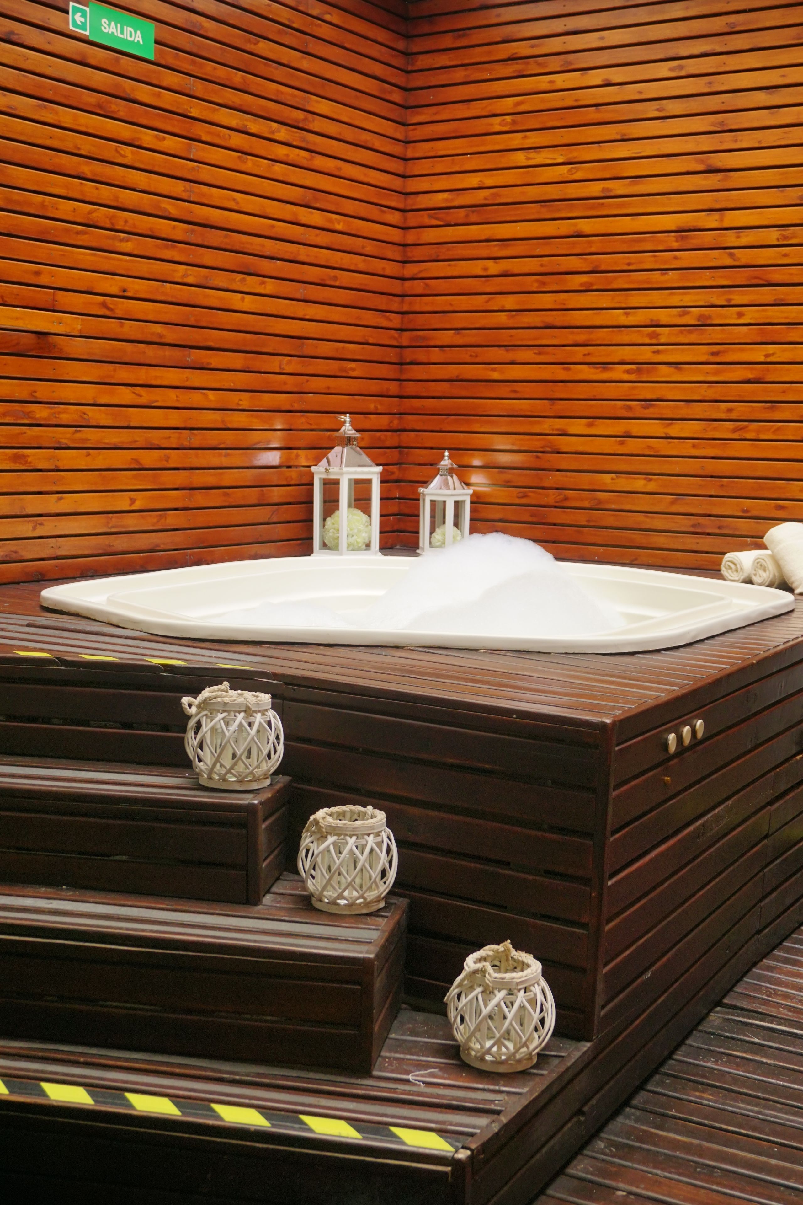 Una bañera de hidromasaje de madera con dos faroles blancos y una toalla en los escalones.