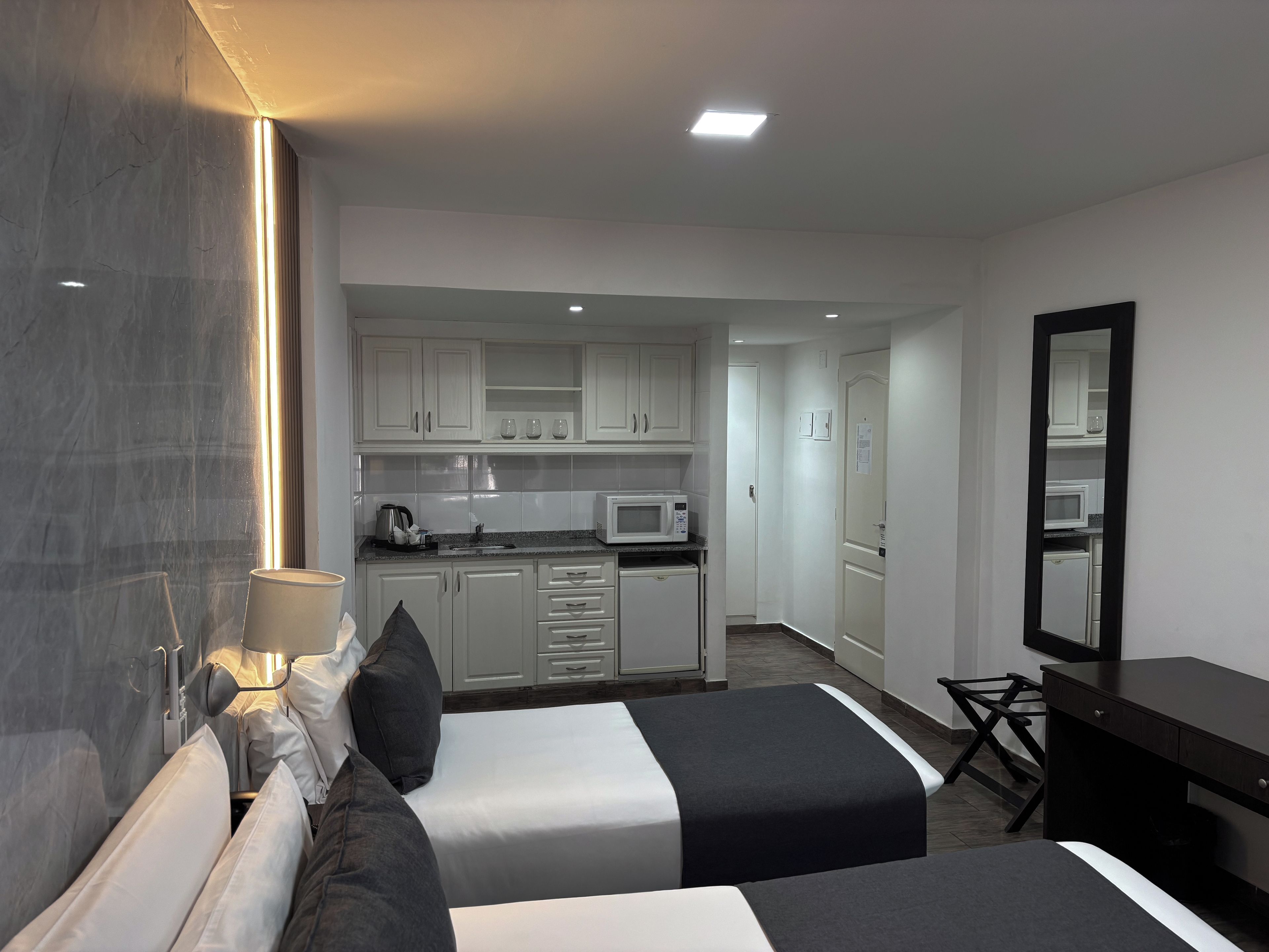 A hotel room with two beds, a desk, a kitchenette, and a bathroom.
