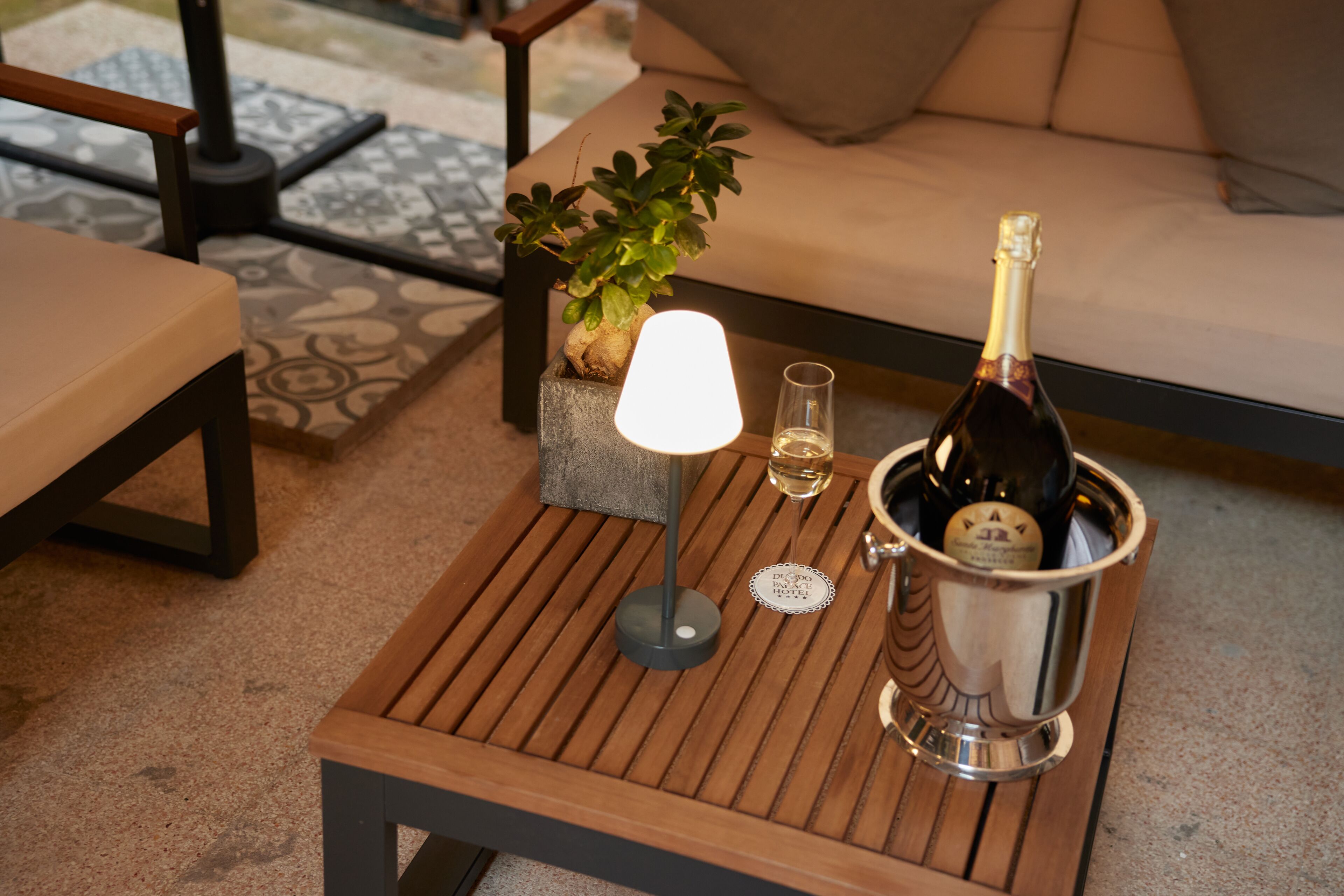 Una mesa de madera con una botella de champán, una copa y una lámpara.