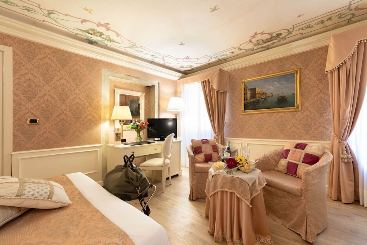 Ein Hotelzimmer mit einem Bett, einem Schreibtisch mit Computer, einem Sessel, einer Couch und einem Tisch mit Blumenvase.