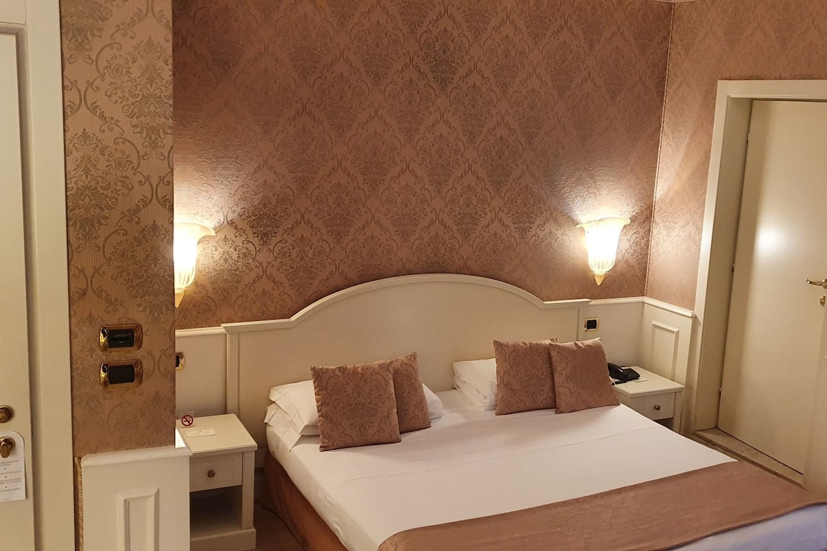Ein Hotelzimmer mit einem großen Bett, zwei Nachttischen, einer Stehlampe und einer Tür.