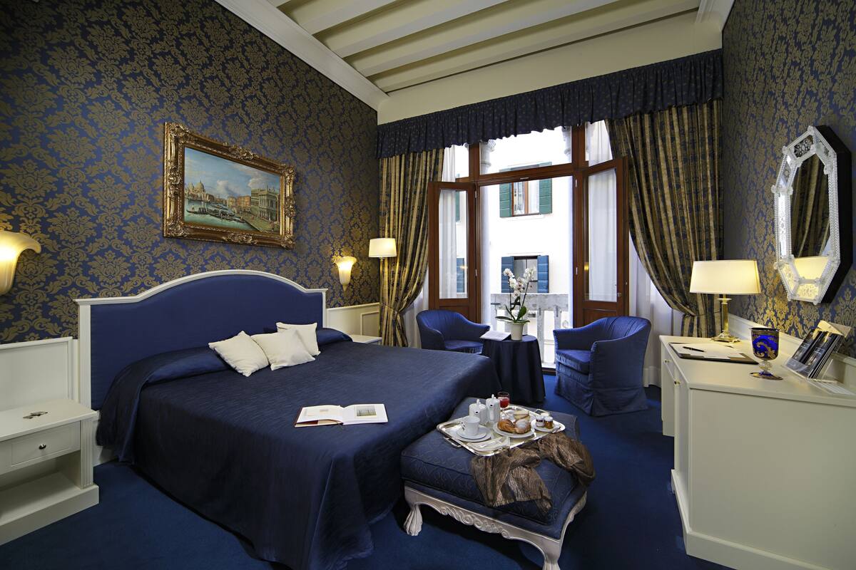 Ein Hotelzimmer mit einem großen Bett, einem Schreibtisch, einem Stuhl und einem kleinen Tisch mit Frühstücksangeboten.