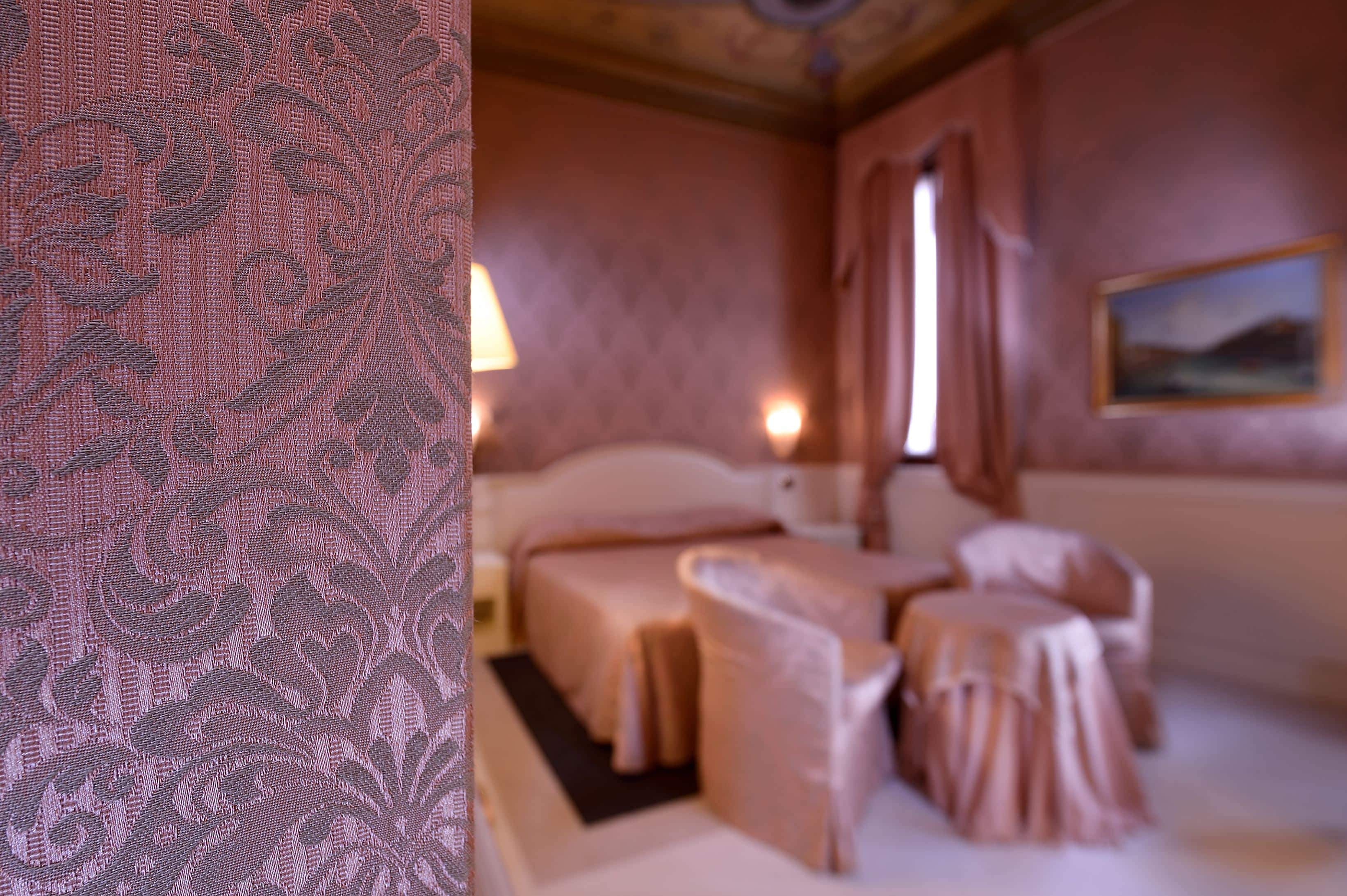 A hotel room with a bed, two chairs, a table, a lamp, and a painting on the wall.