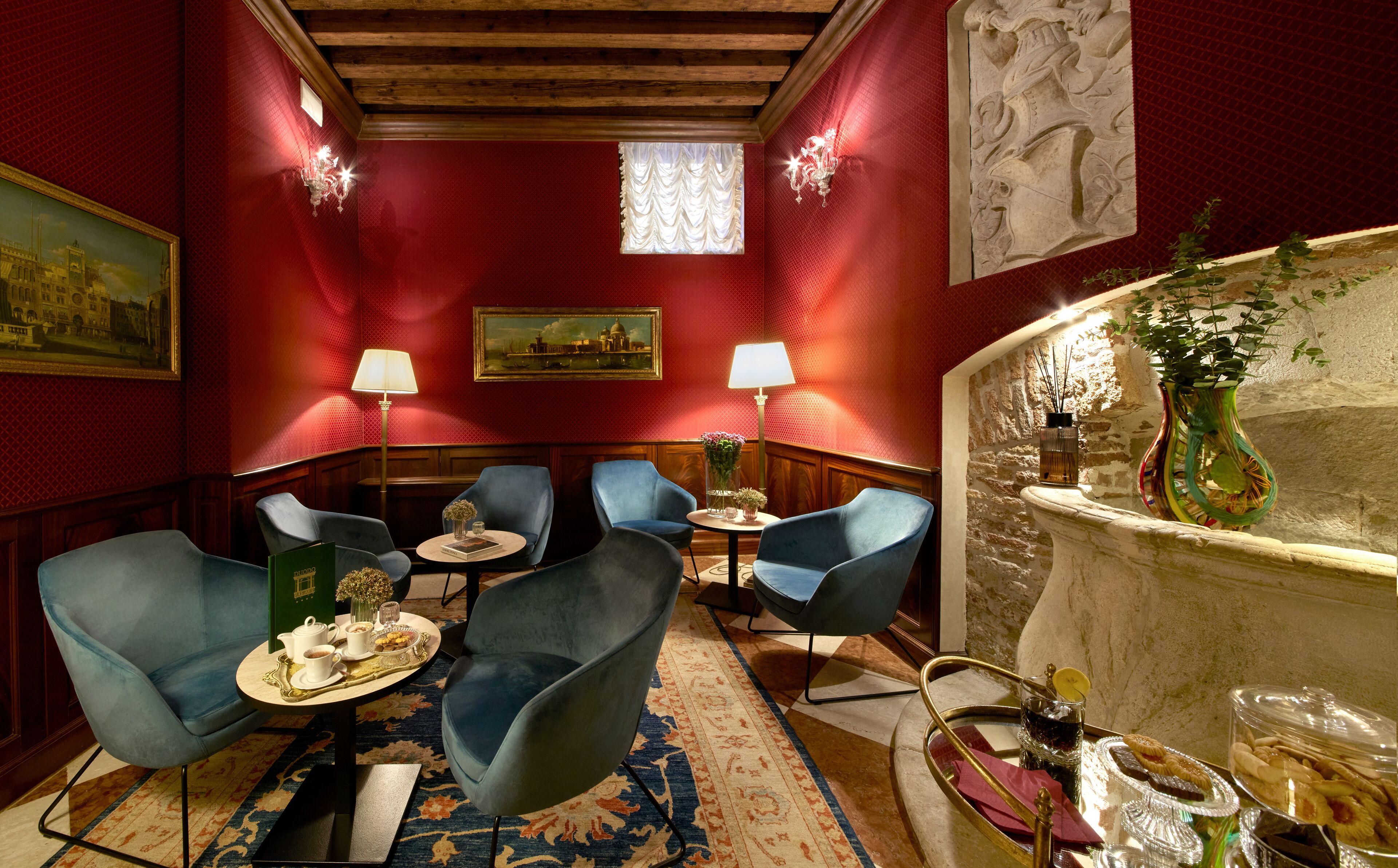 A room with red walls, blue chairs, a small table with a tray of food, and a vase with flowers.