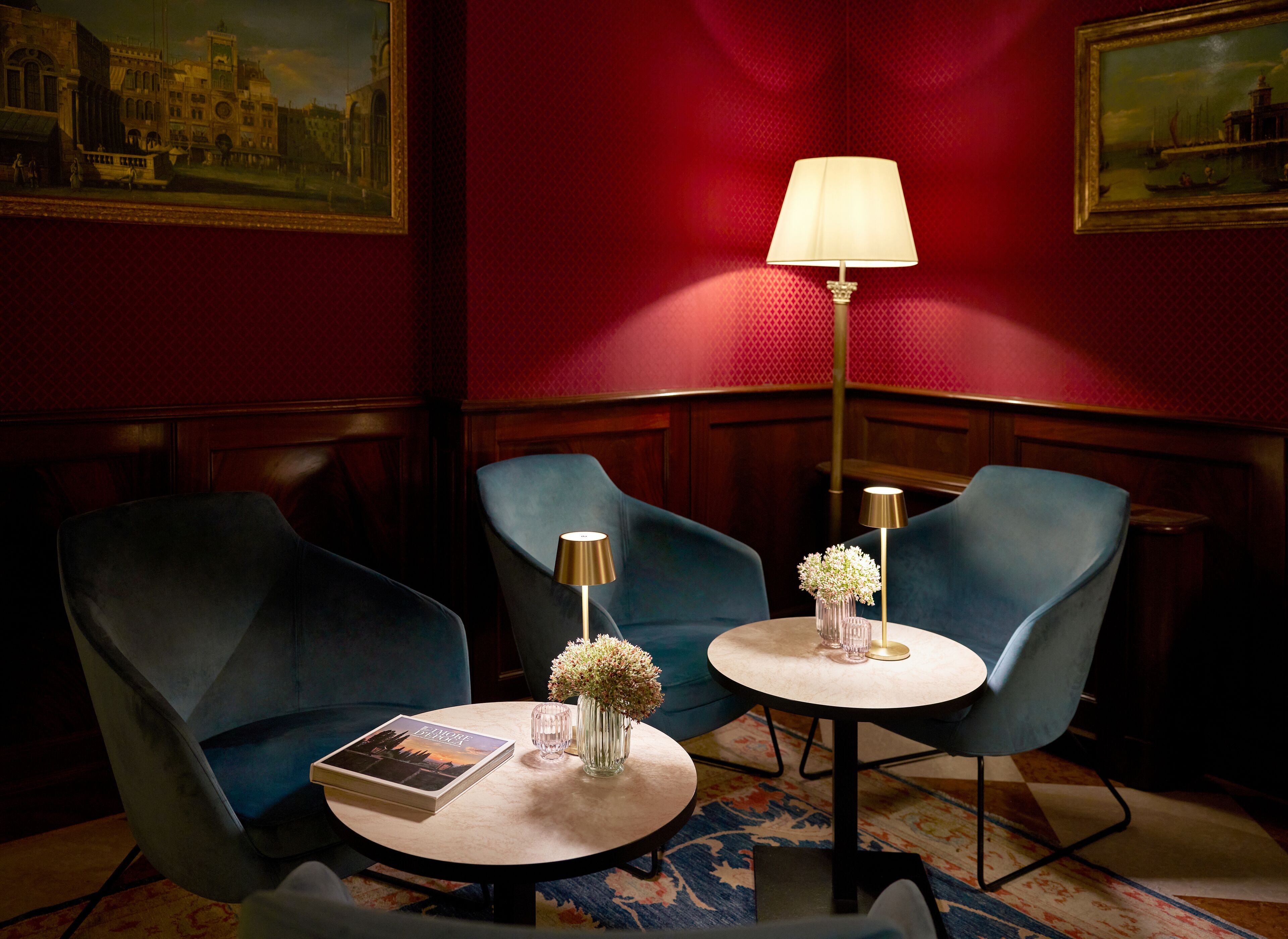 A room with two blue armchairs, a round table with a book and a vase of flowers, and two floor lamps.