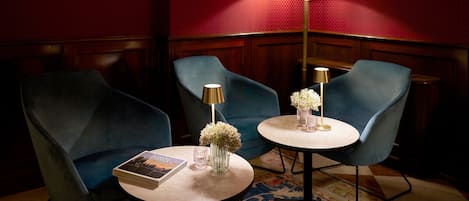 A room with two blue armchairs, a round table with a book and a vase of flowers, and two floor lamps.