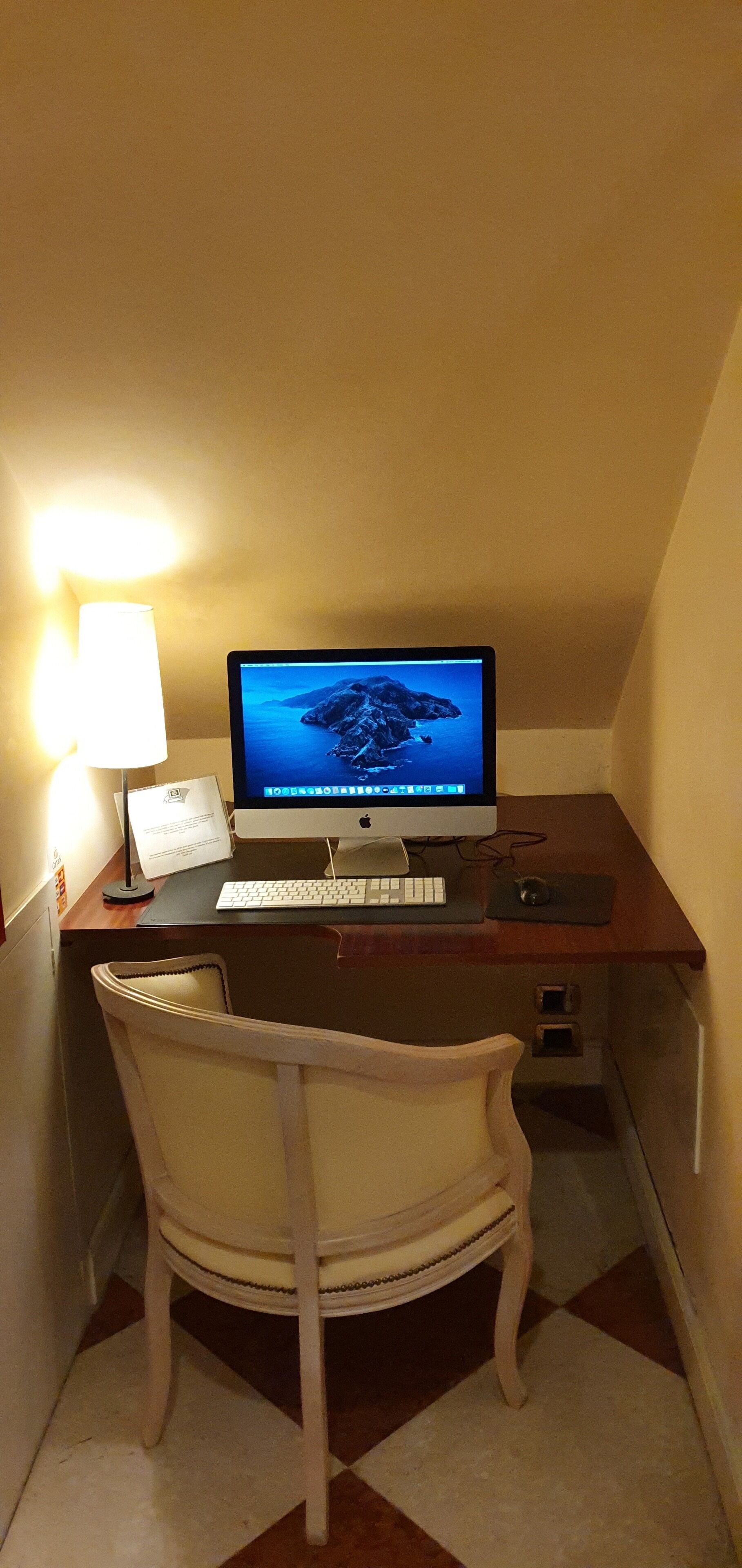 A corner desk with a computer, keyboard, mouse, and a lamp.