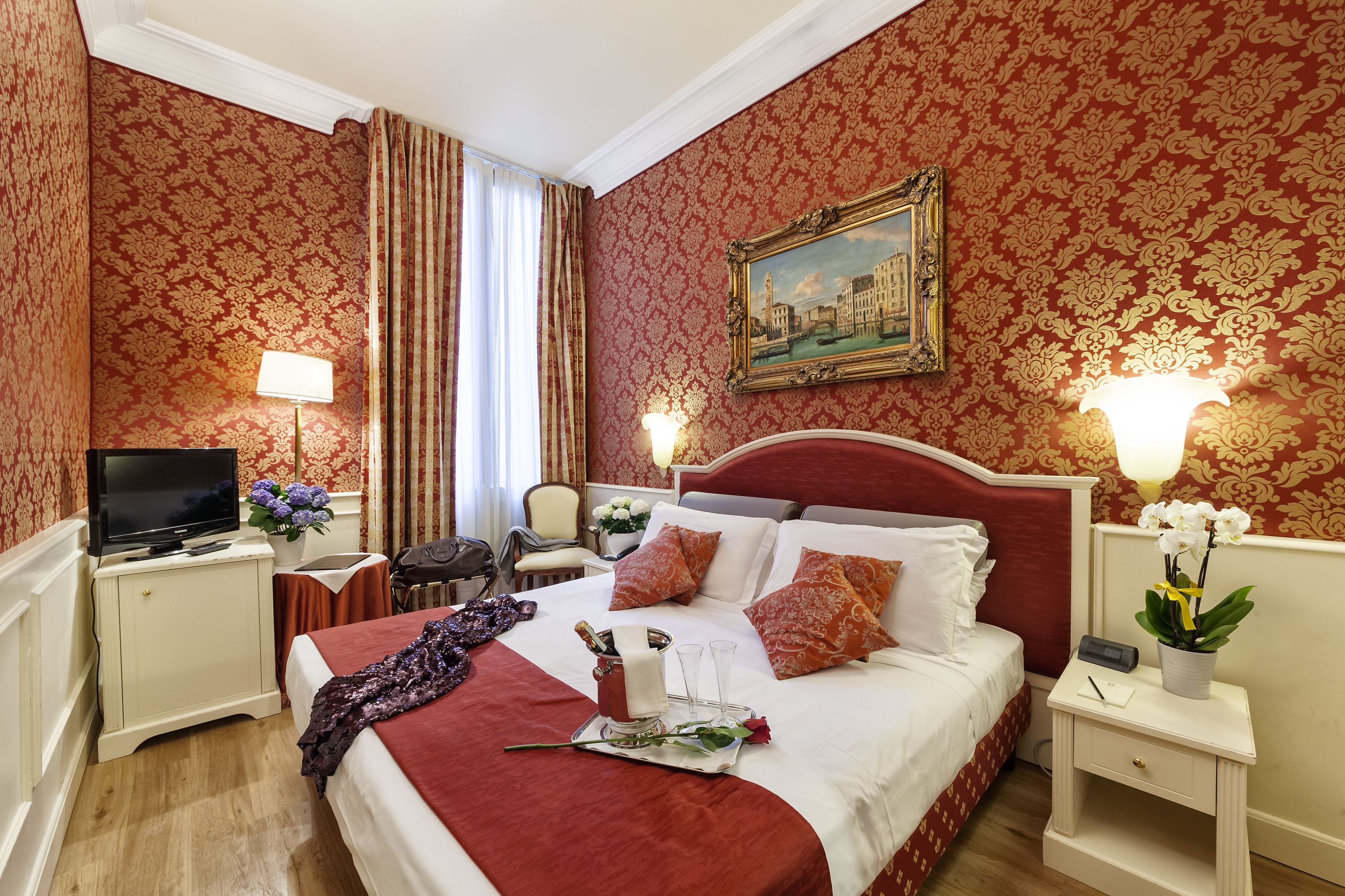 A hotel room with a large bed, two bedside tables, a TV, and a painting on the wall.