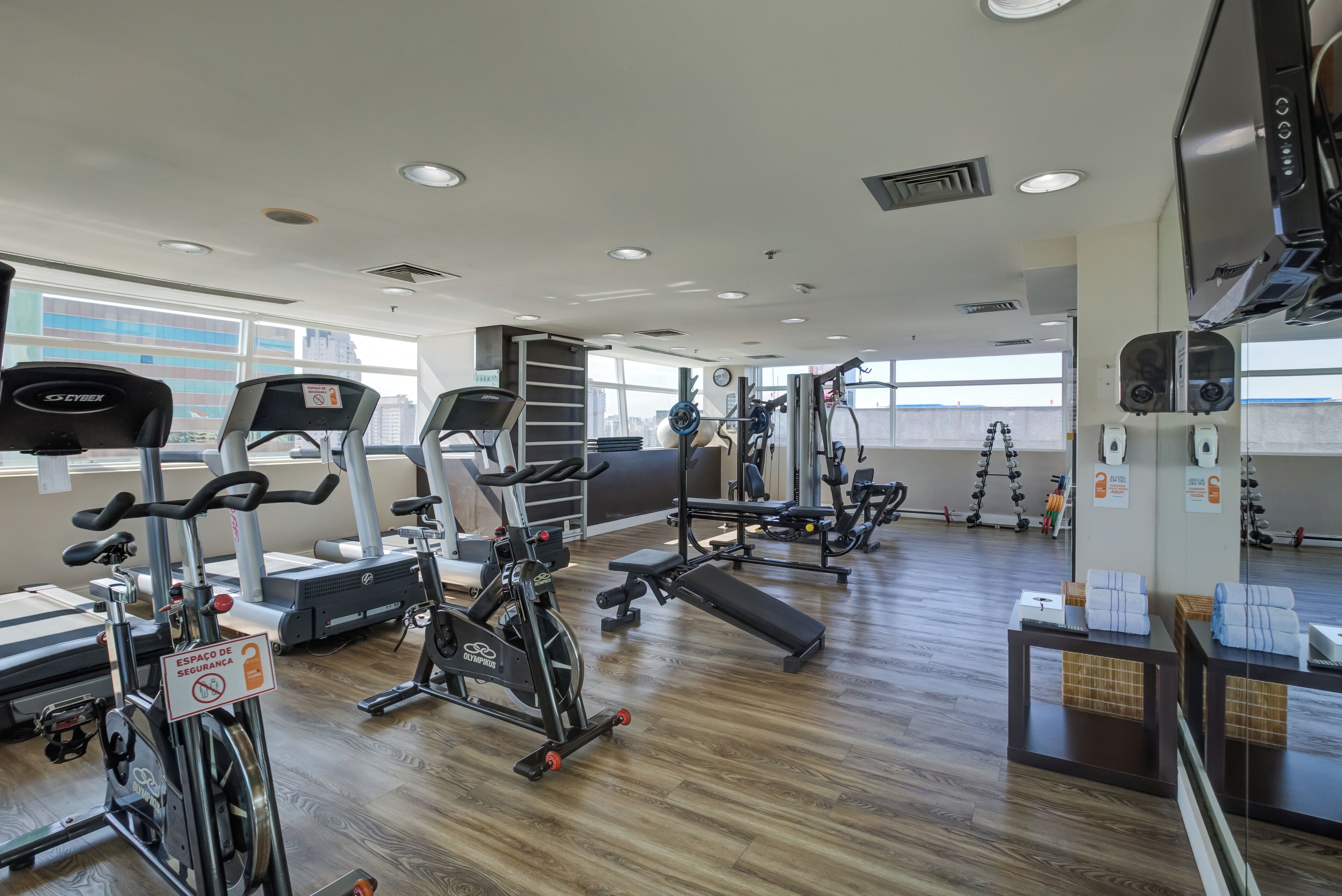 A gym with various exercise equipment, wooden flooring, and large windows.