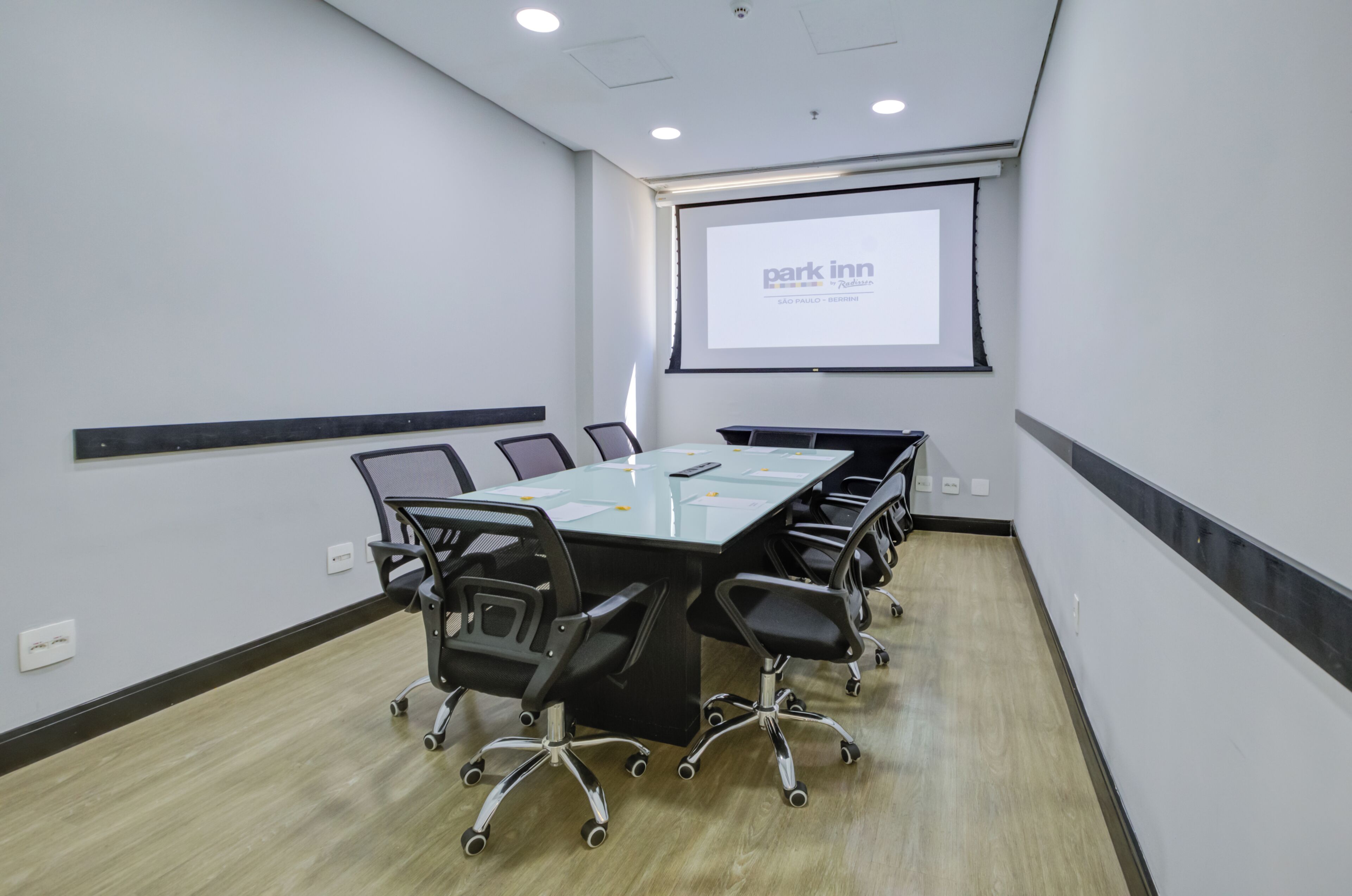 A conference room with a long table, chairs, a projector screen, and a presentation screen.