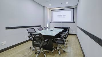 A conference room with a long table, chairs, a projector screen, and a presentation screen.