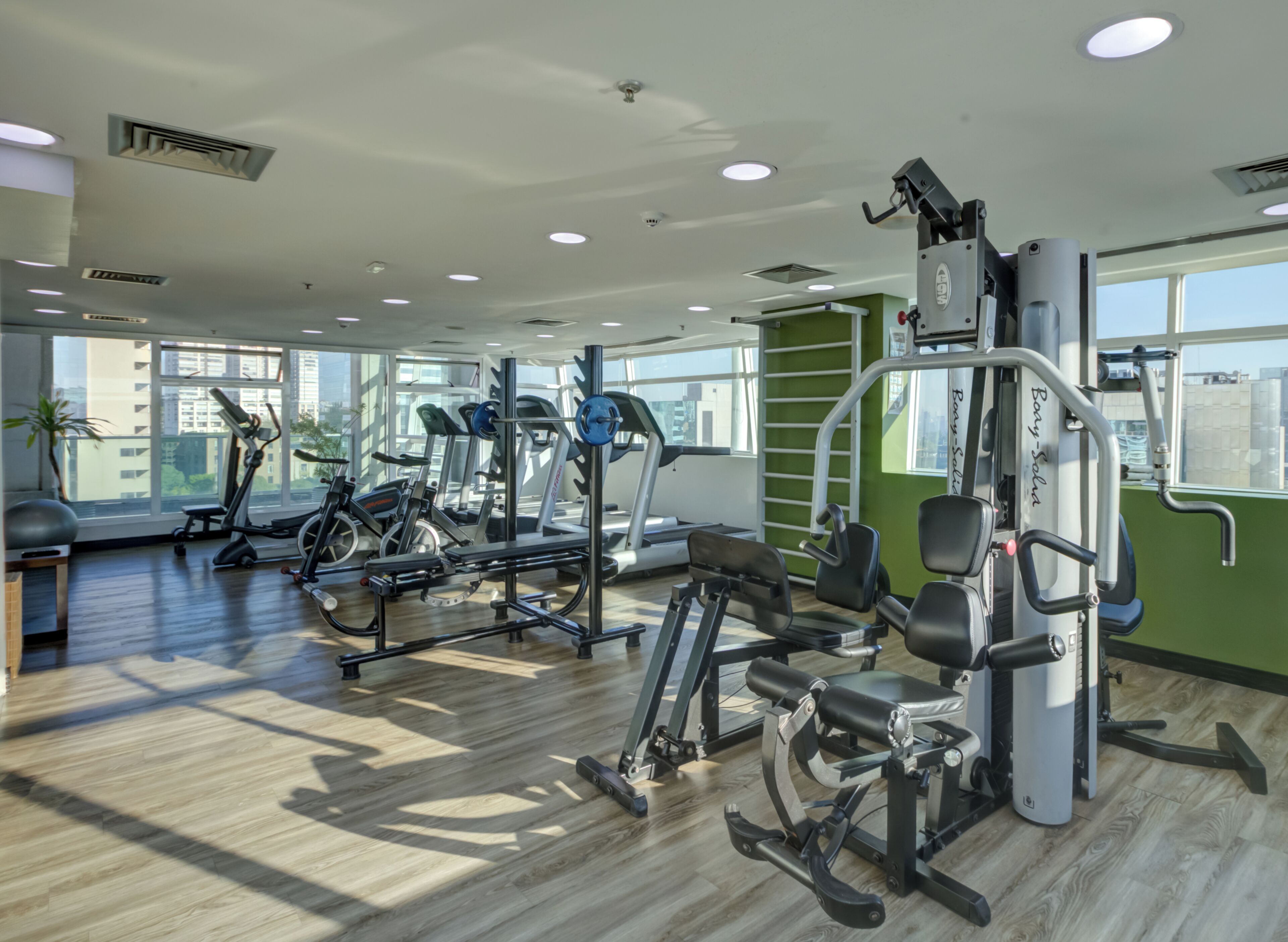 Une salle de sport équipée de divers appareils d’exercice, dotée de grandes fenêtres et d’un plancher en bois.
