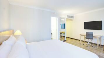 Une chambre d’hôtel avec un grand lit, un bureau, une chaise, une télévision et une salle de bain visible à travers une porte ouverte.