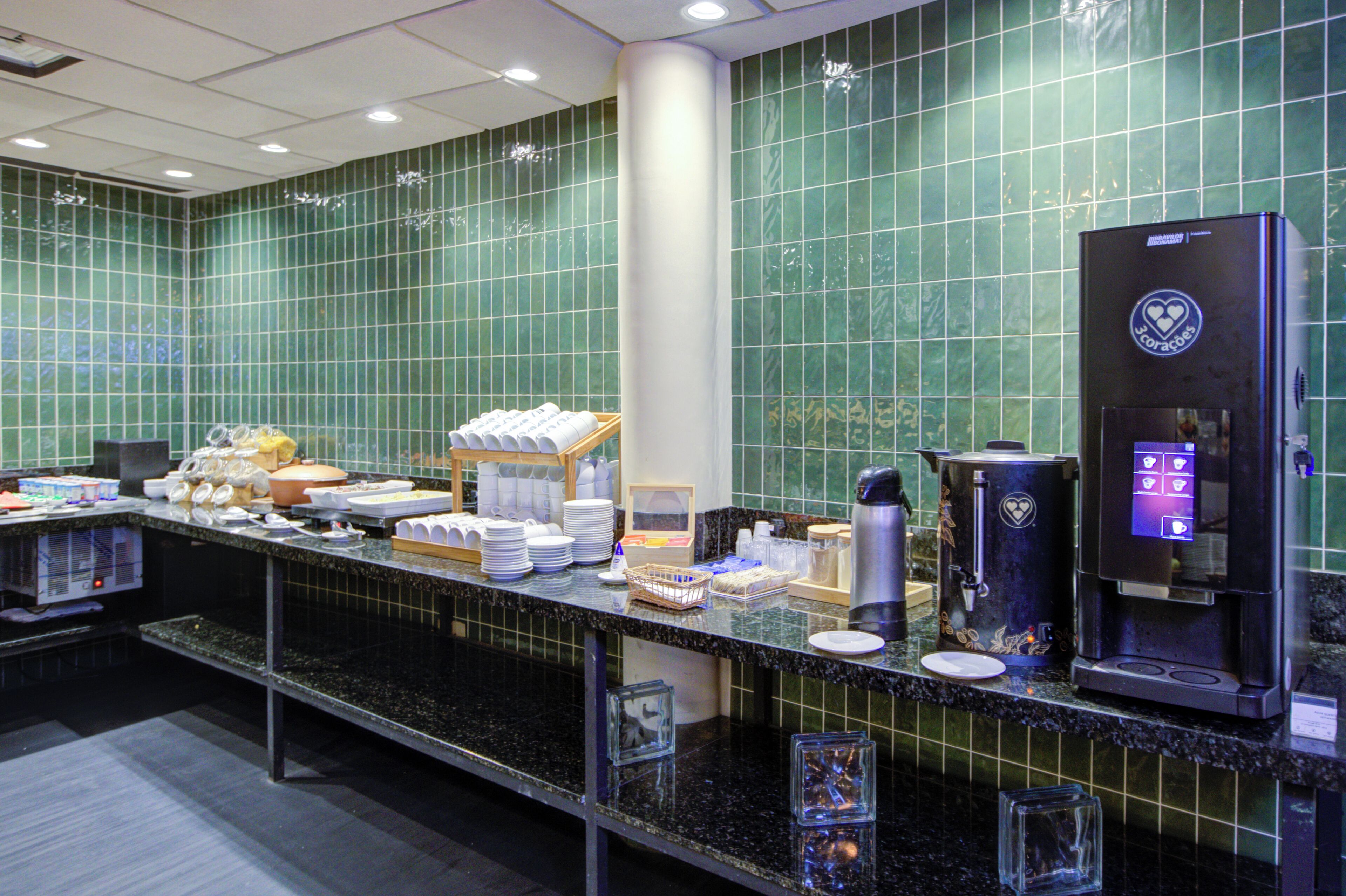 Un espace pour le petit-déjeuner à l’hôtel, avec un coin café en libre-service, un buffet proposant divers plats et une crédence carrelée.