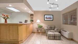 A reception area with a wooden desk, a couch, a lamp, and a framed picture on the wall. - North Platte Inn & Suites (North Platte)