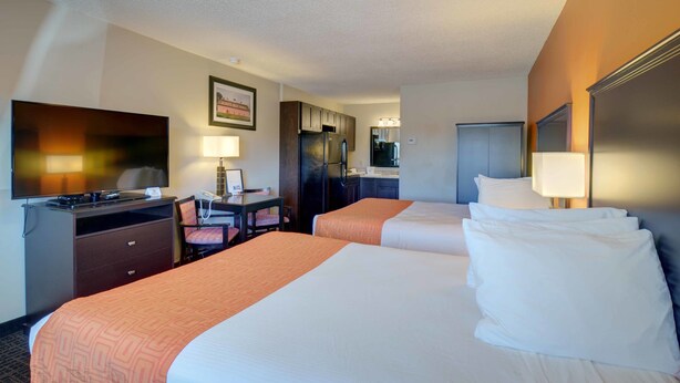 A hotel room with two beds, a desk with a chair, a television, and a kitchenette. - North Platte Inn & Suites (North Platte)