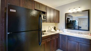 A kitchen with dark wooden cabinets, a black refrigerator, a built-in oven, a sink, and a large mirror above the countertop. - North Platte Inn & Suites (North Platte)