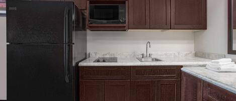 A kitchen with dark wooden cabinets, a black refrigerator, a microwave, and a sink.