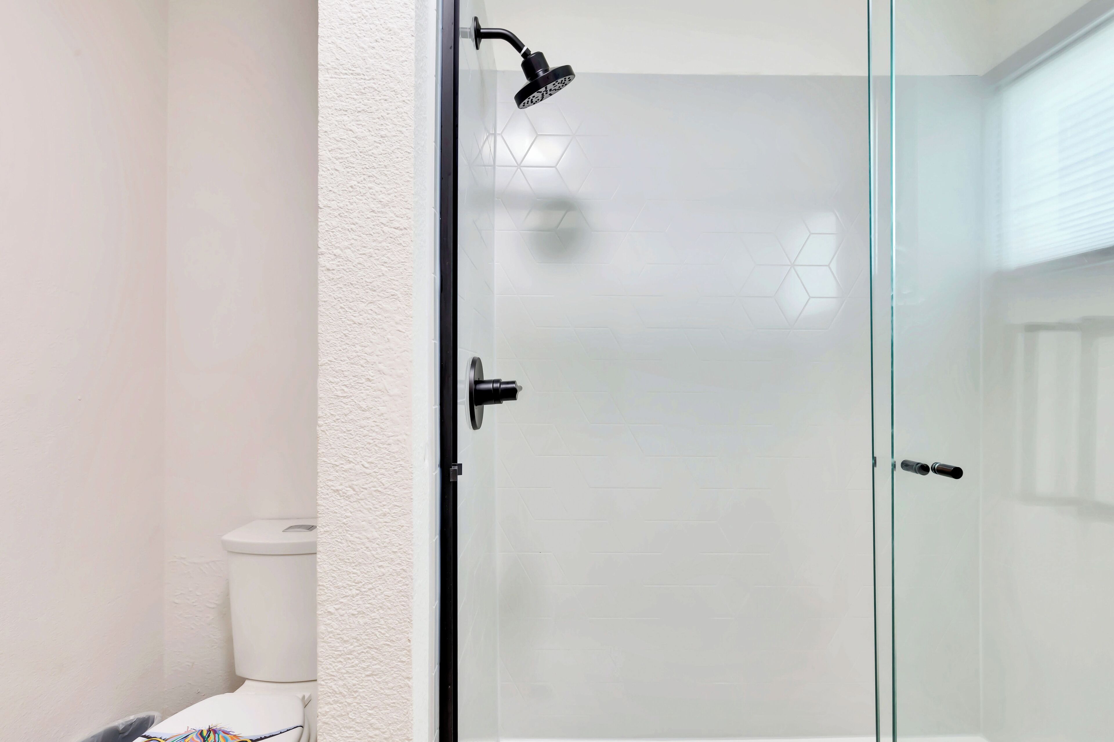 Une salle de bain moderne avec une douche à parois de verre, des carreaux blancs et des toilettes blanches.
