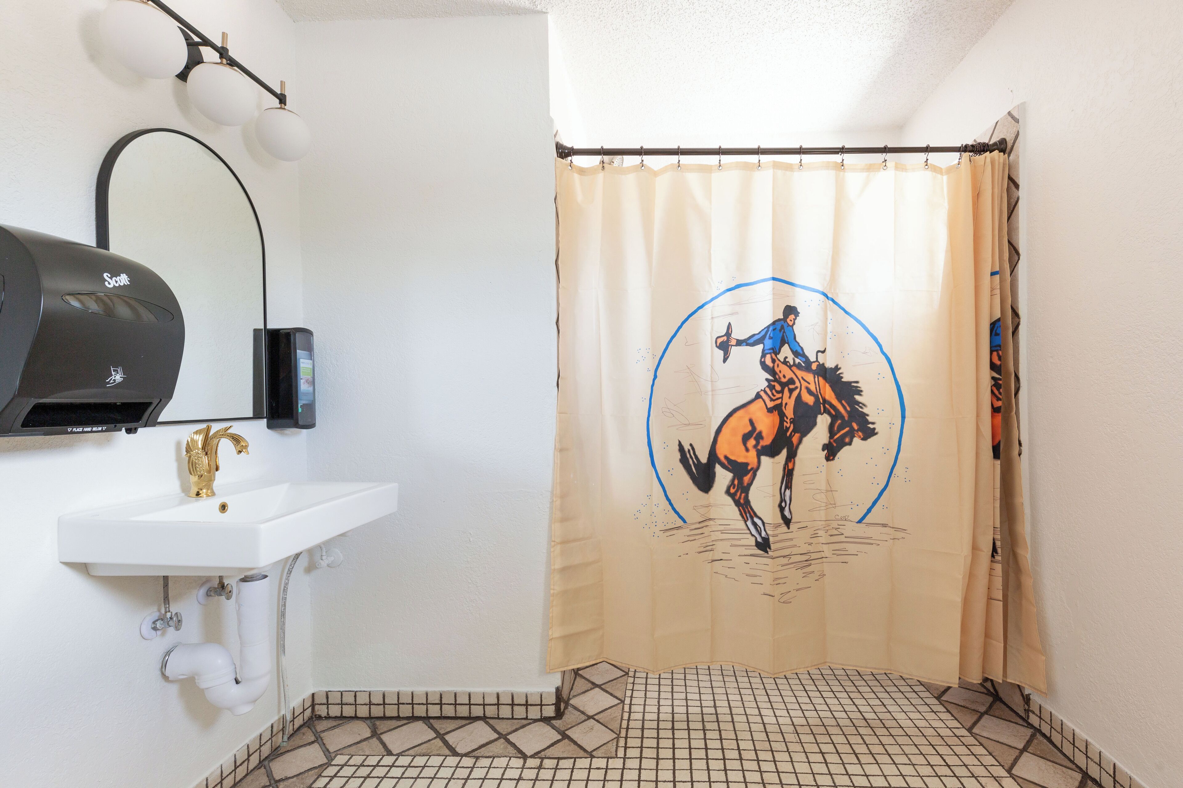 A bathroom with a white sink, a towel dispenser, and a shower curtain with a horse and rider design.