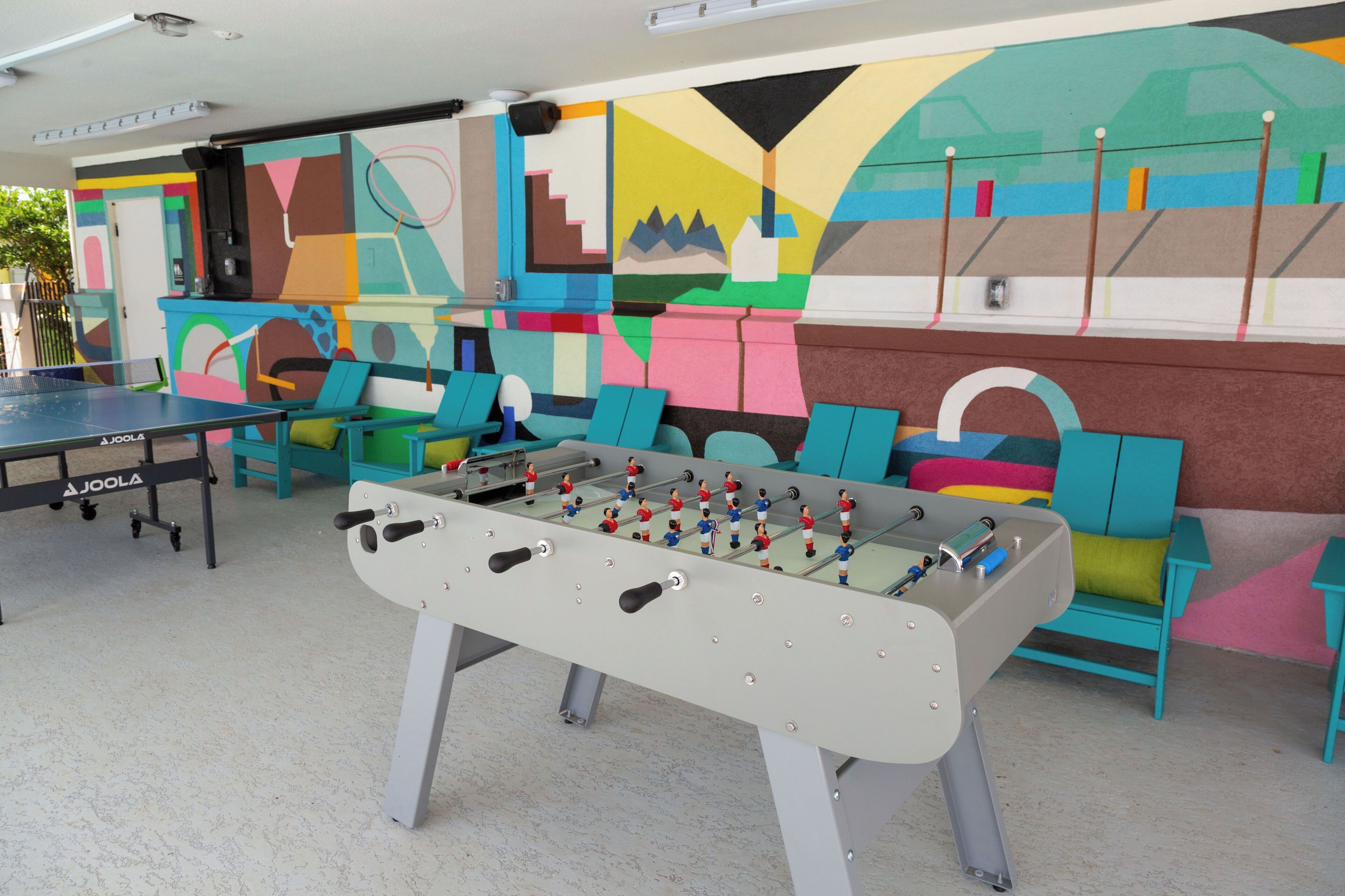 A foosball table in a room with colorful chairs and a wall mural.