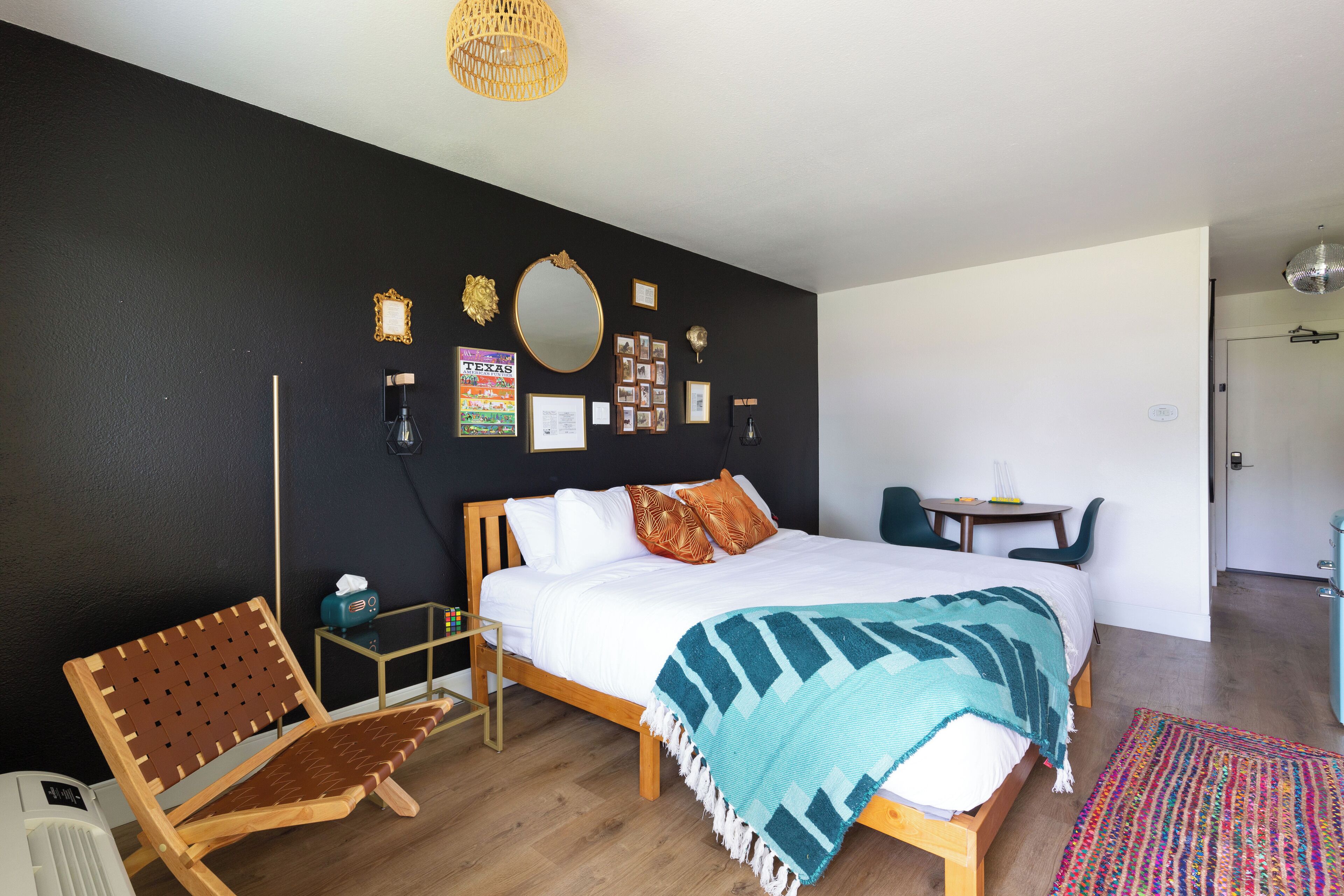 A bedroom with a bed, a chair, a small table, and a wall decorated with pictures and a mirror.