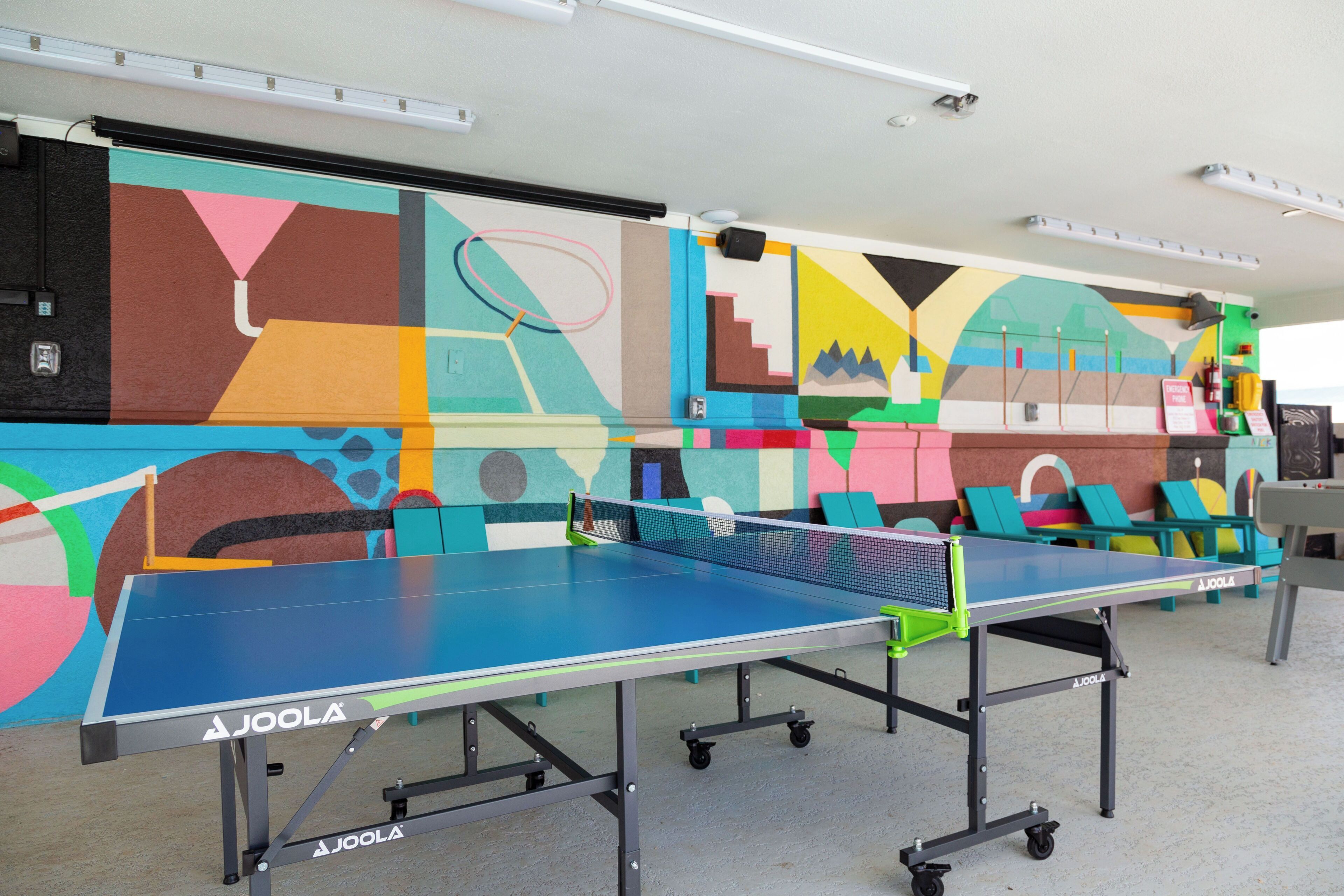 Una mesa de ping pong con un mural colorido al fondo.