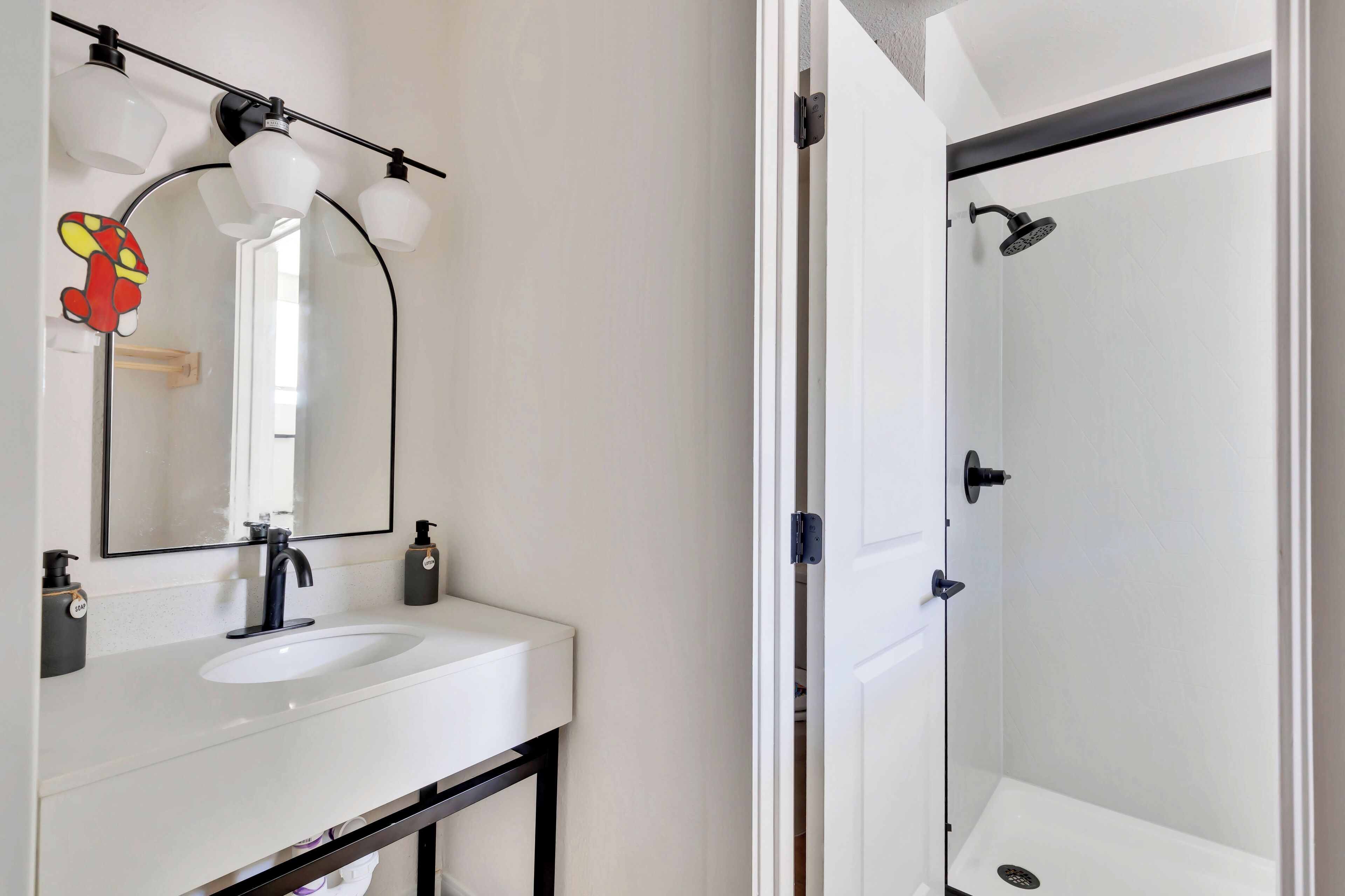 Un baño con un lavamanos blanco, grifo negro y un espejo con tres luces.