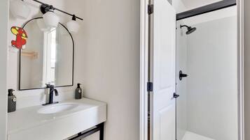 Un baño con un lavamanos blanco, grifo negro y un espejo con tres luces.