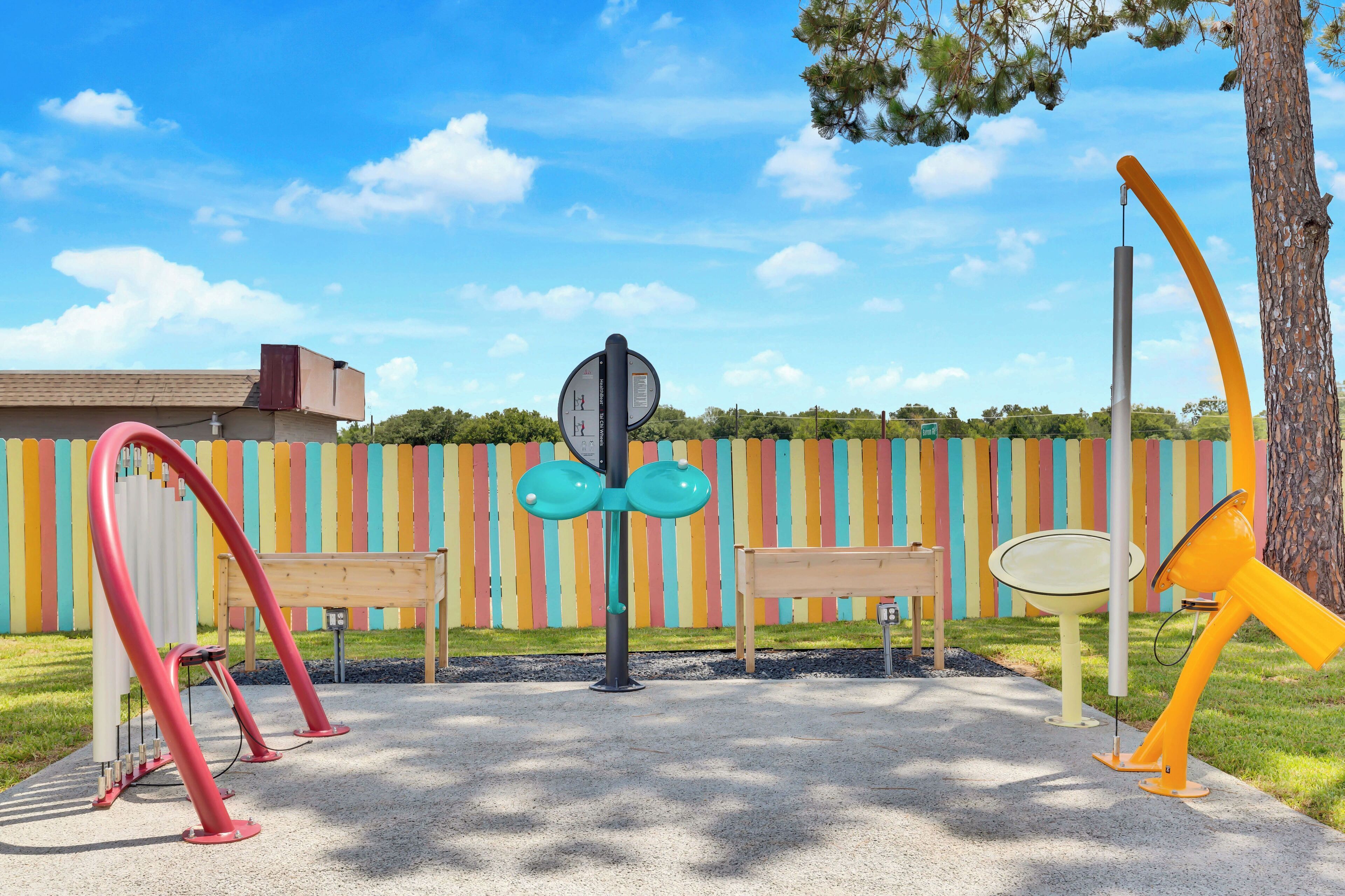 Un parque infantil con columpios y un tobogán, un banco y una valla de colores al fondo.