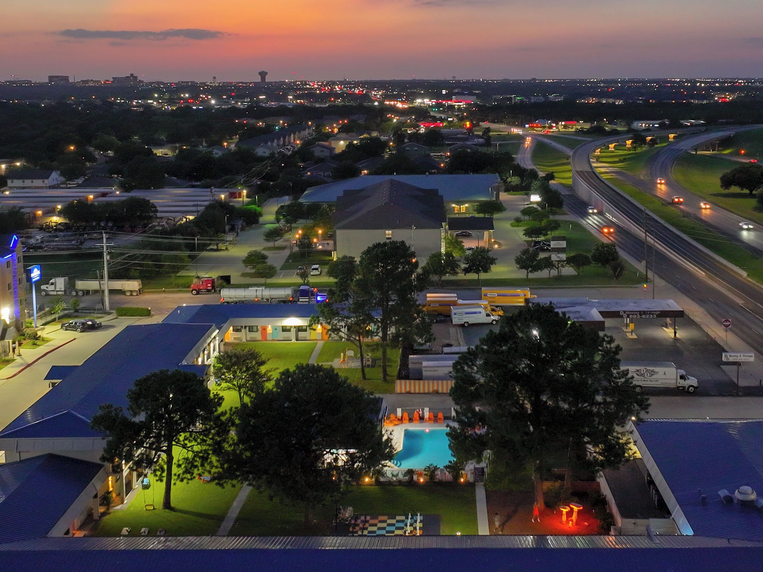 Um hotel com piscina, estacionamento e vista para o horizonte urbano ao anoitecer.