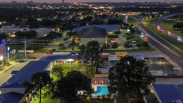 Um hotel com piscina, estacionamento e vista para o horizonte urbano ao anoitecer.