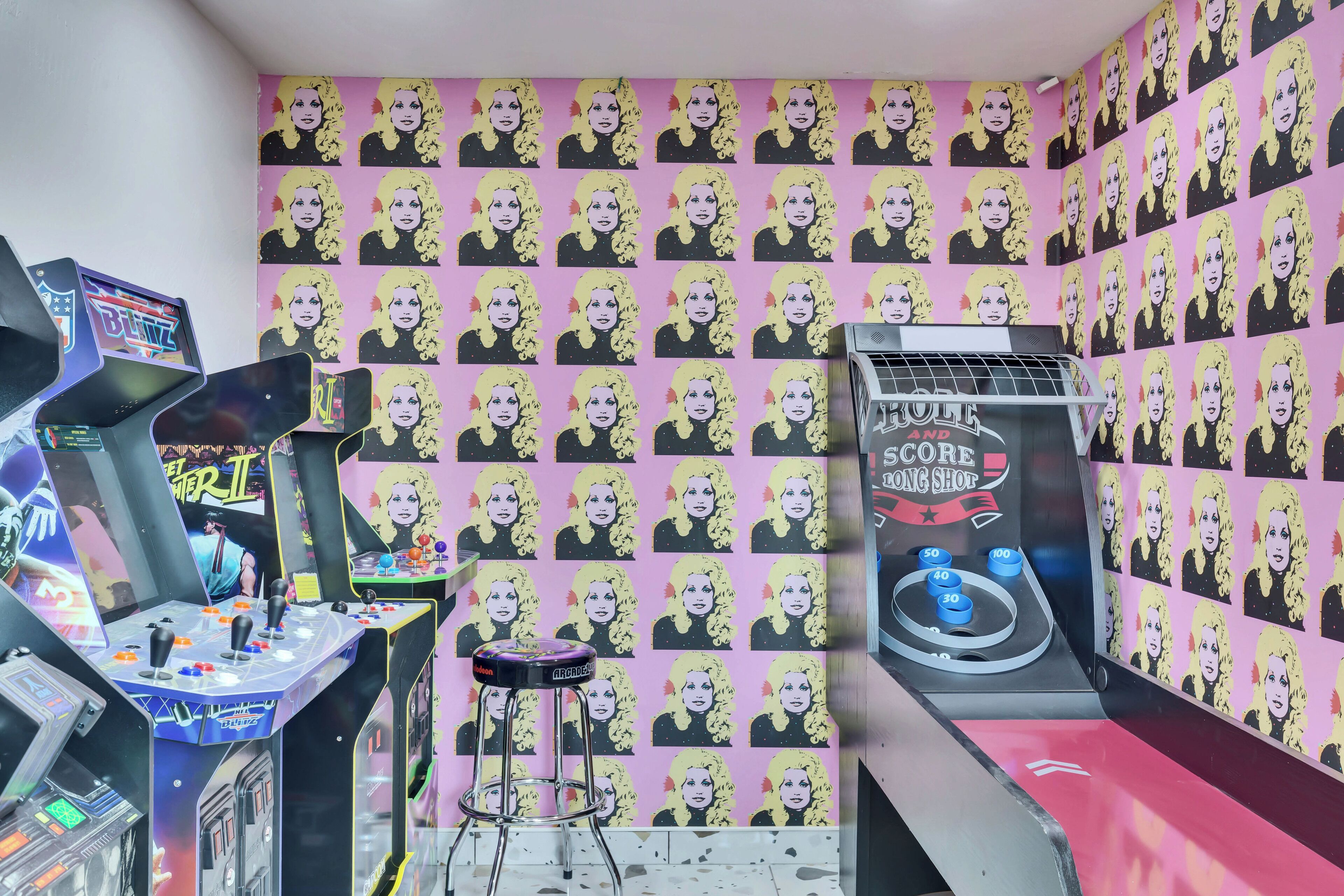 A room with arcade machines, a stool, and a wall covered with repeated images.