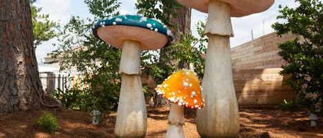 Three mushroom-shaped sculptures in a garden setting with trees and a brick wall in the background.