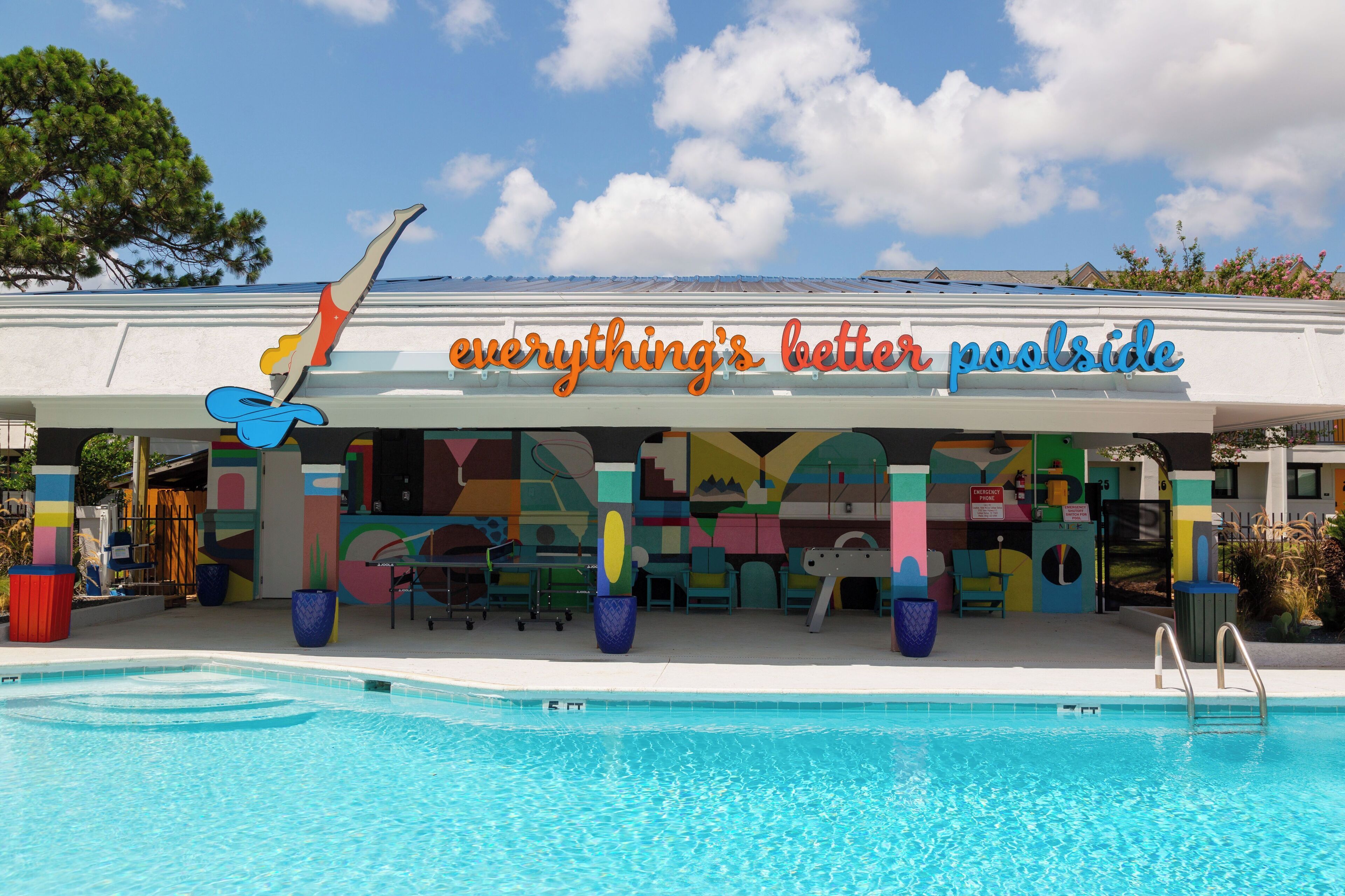 A poolside area with a colorful mural and a sign that reads "everything's better poolside."