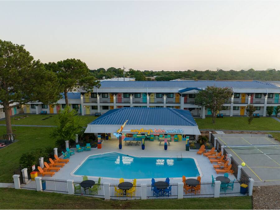 Un hotel con piscina, mobiliario exterior y una fachada colorida.