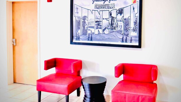 A room with two red chairs, a black round table, and a framed picture of a cityscape on the wall.