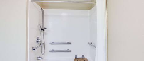 A white bathtub with a wooden tray, two handrails, and a showerhead.